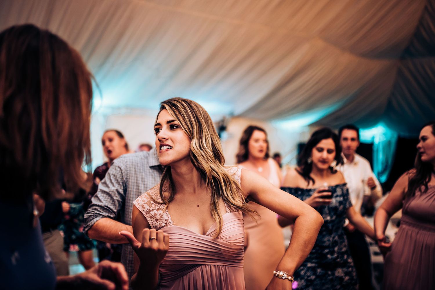 Wedding guests enjoy dancing and festivities under an elegantly lit reception tent.
