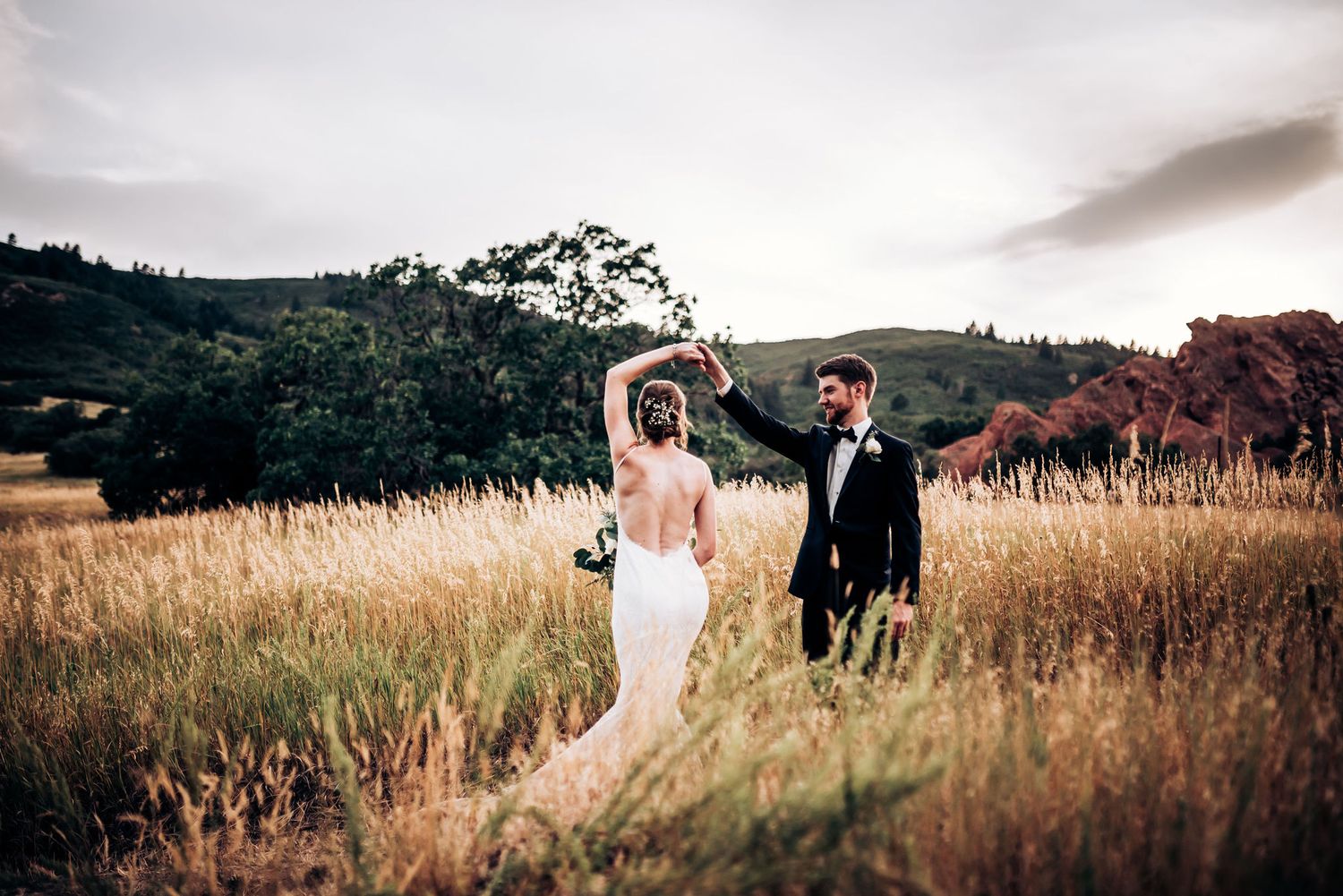 Couple celebrates in golden meadow with bride's dress flowing in evening light.