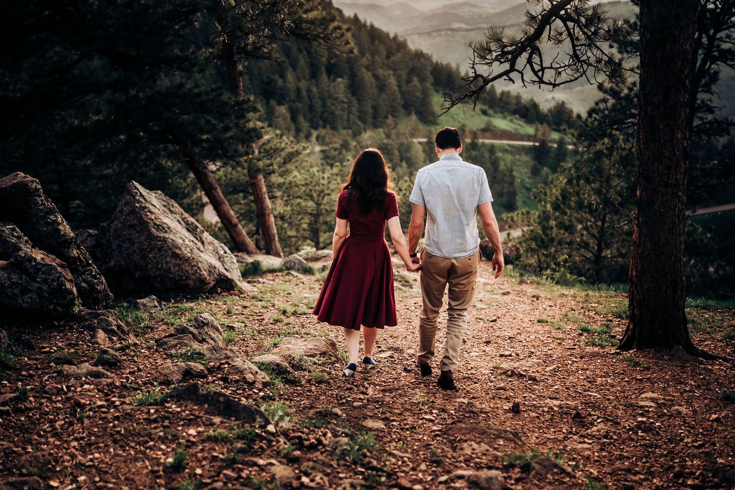 Couple holding hands while walking on mountain trail through pine forest.
