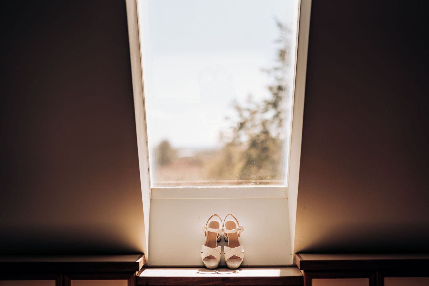 Wedding shoes sit in silhouette against bright window light.