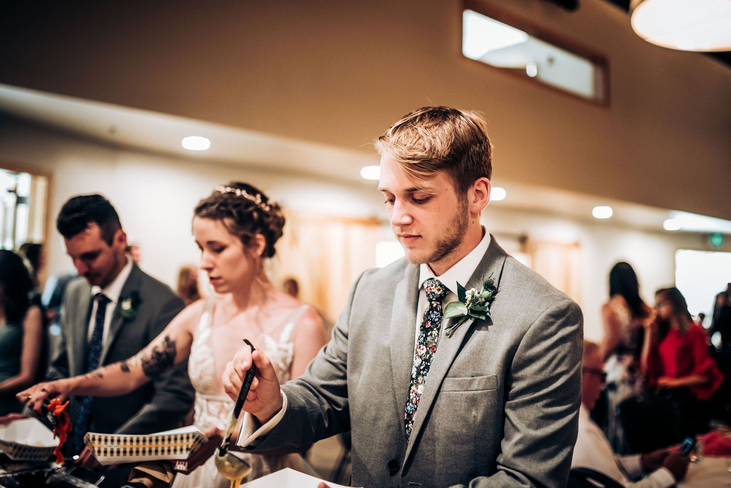 Wedding reception guests serving food at a buffet table under warm lighting.