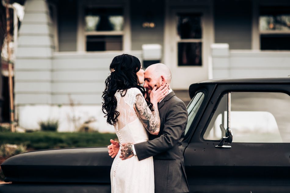 Newlyweds embrace beside classic black car during intimate outdoor wedding shoot.