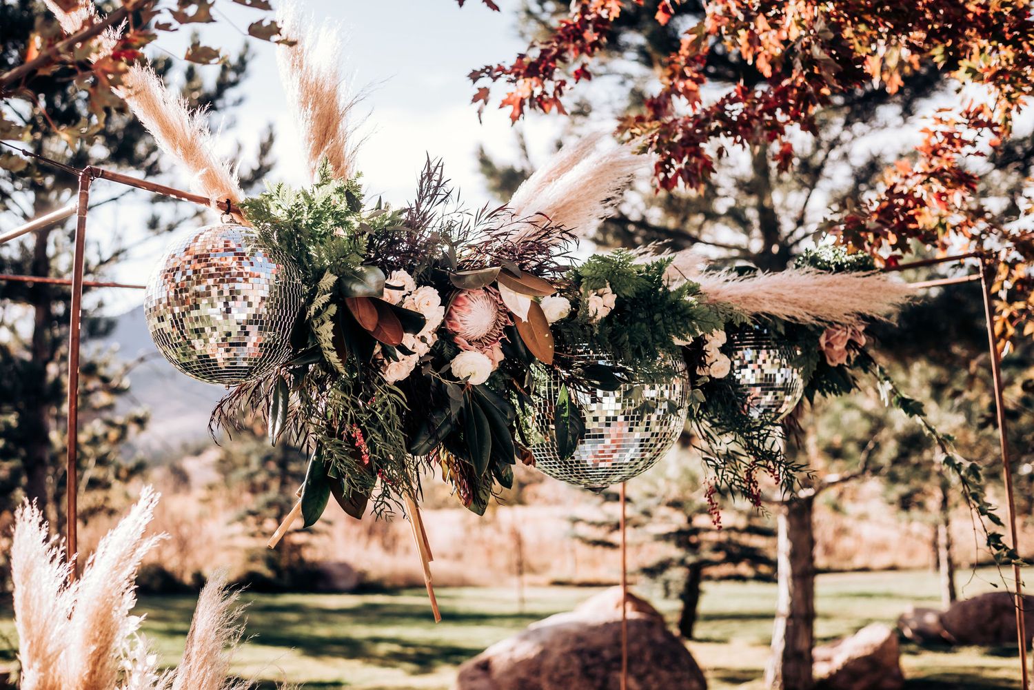 Bohemian wedding decor featuring suspended floral arrangements with pampas grass against autumn trees.