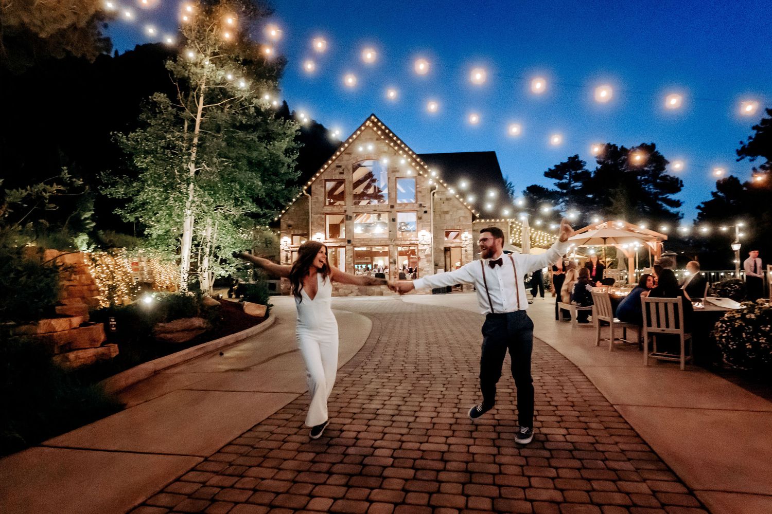 A couple celebrates on a brick pathway in front of an illuminated rustic venue.