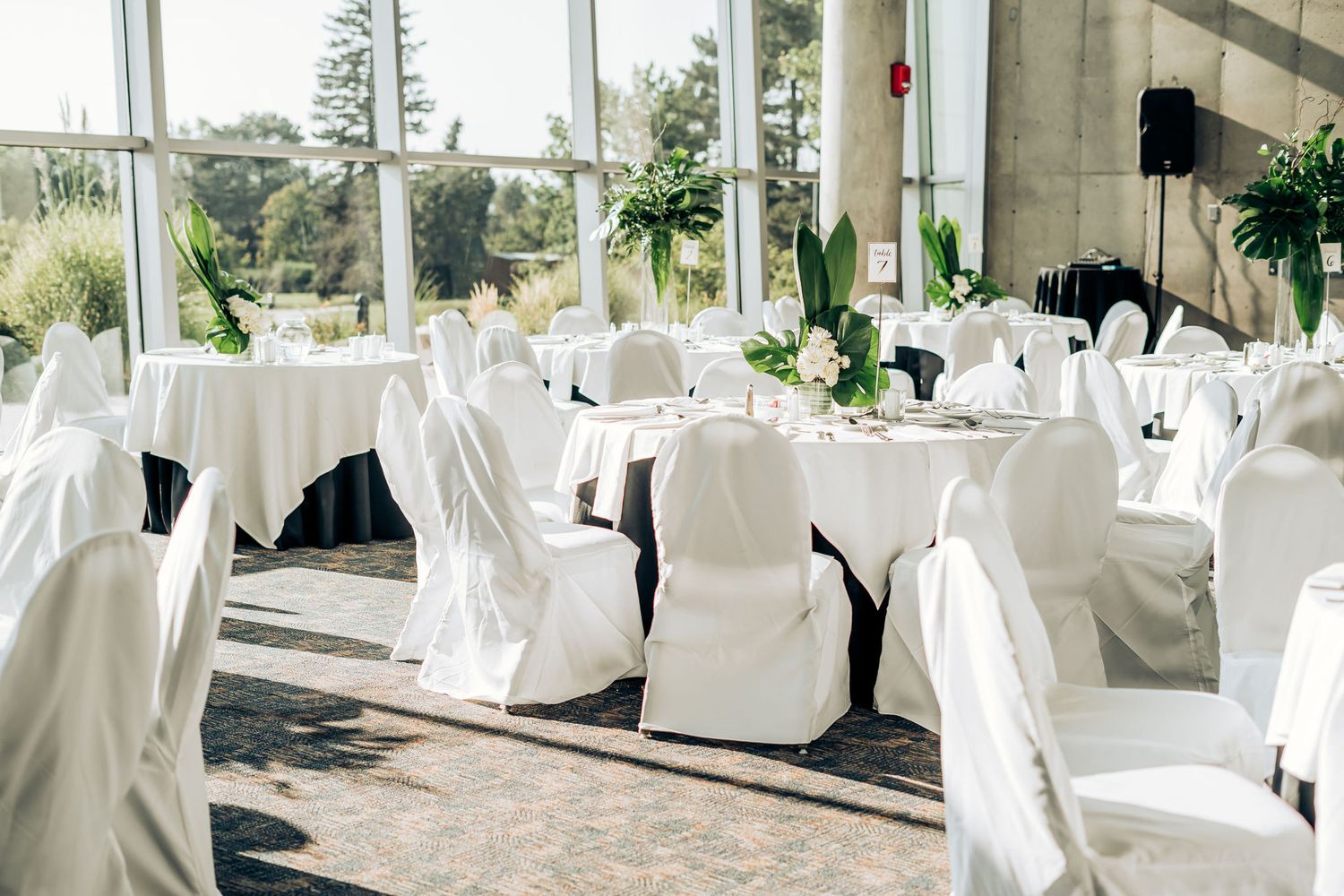 Elegant wedding reception setup with white-covered chairs and tropical centerpieces in a bright venue.