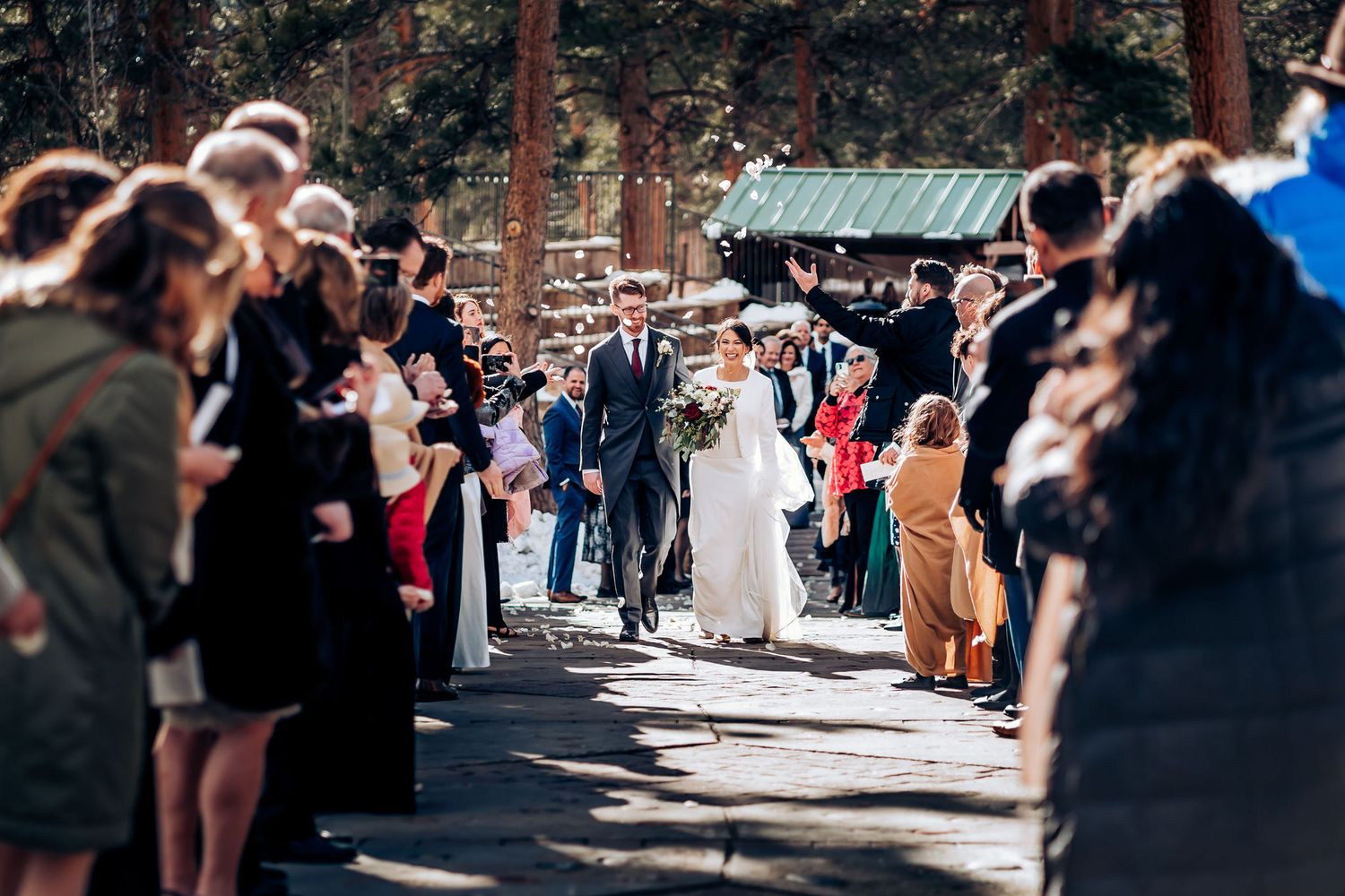 Wedding ceremony procession with guests lining path through wooded area.