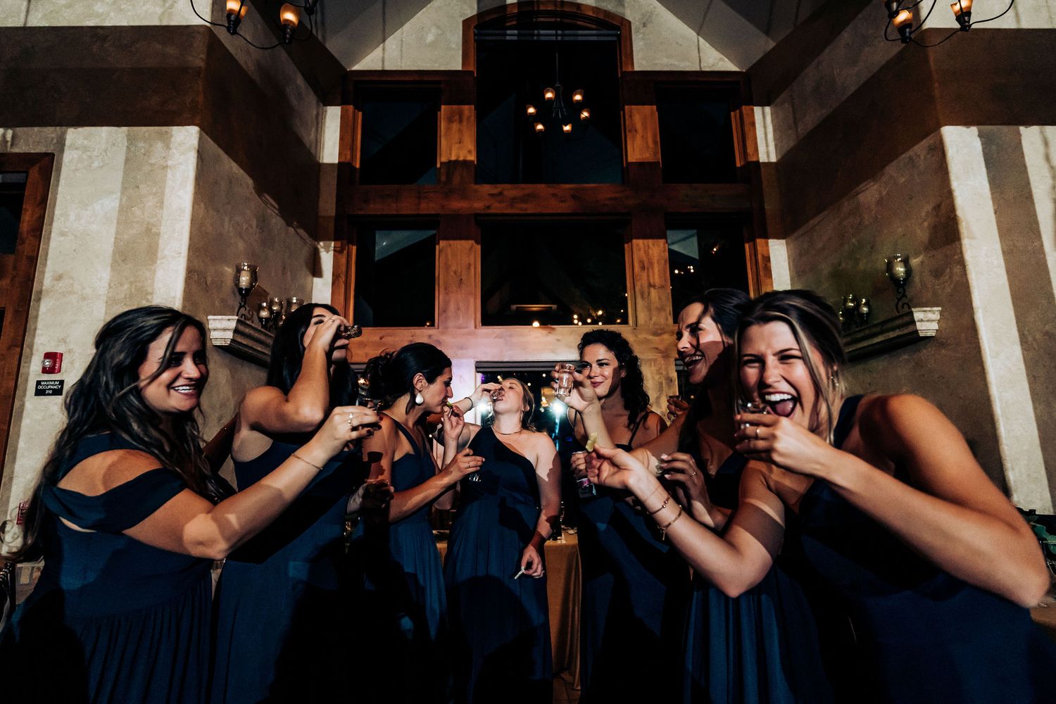 Bridesmaids in navy dresses pose together making fun expressions in rustic church setting.