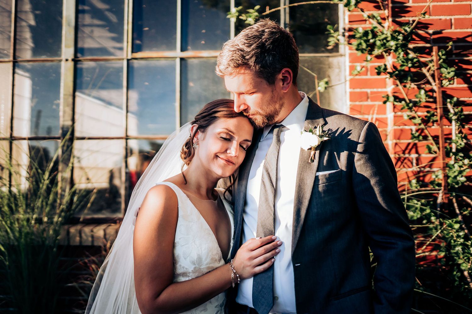 Couple shares a romantic moment against a brick and glass building backdrop.