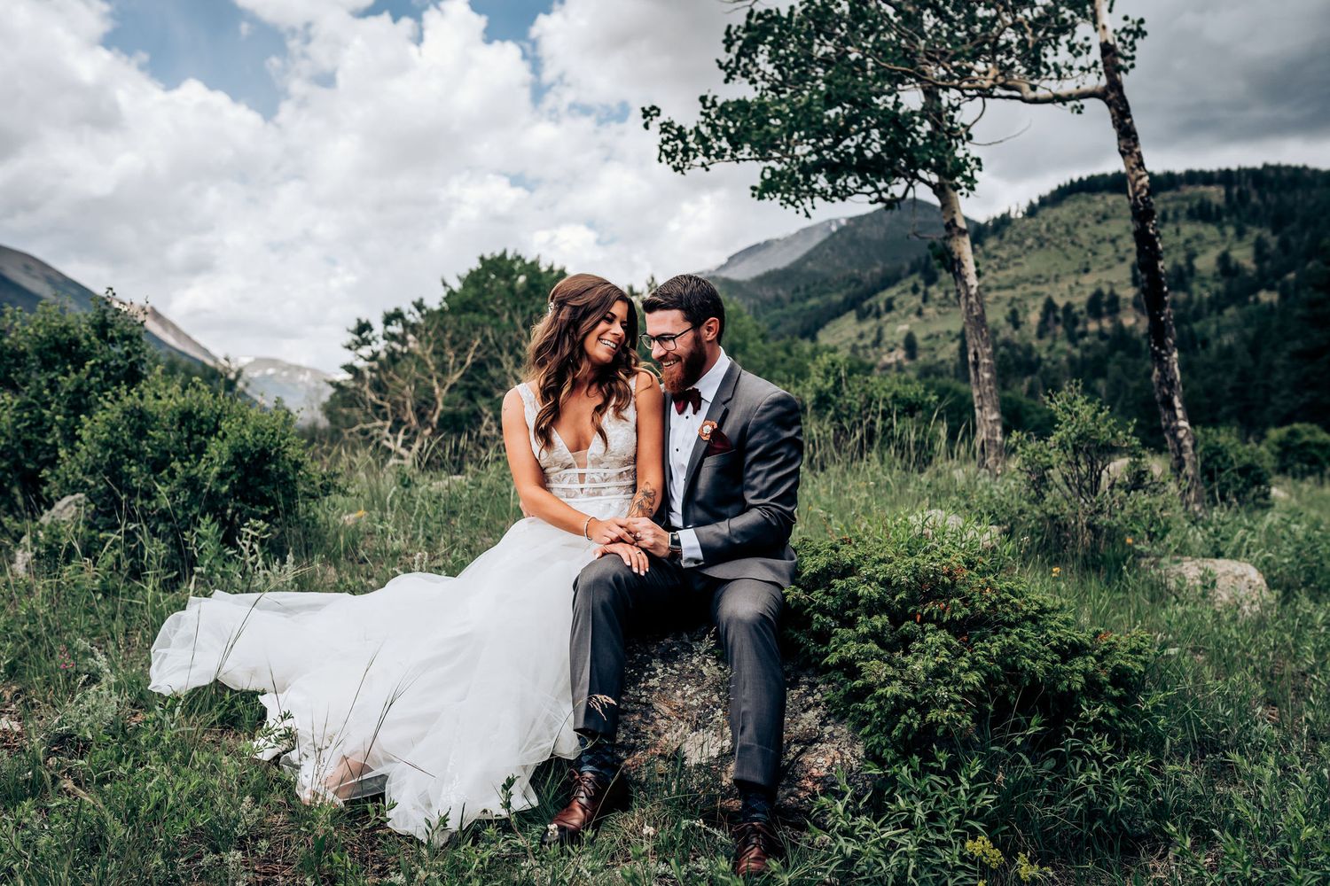 A romantic wedding couple sits together in the mountains surrounded by lush greenery and scenic views.