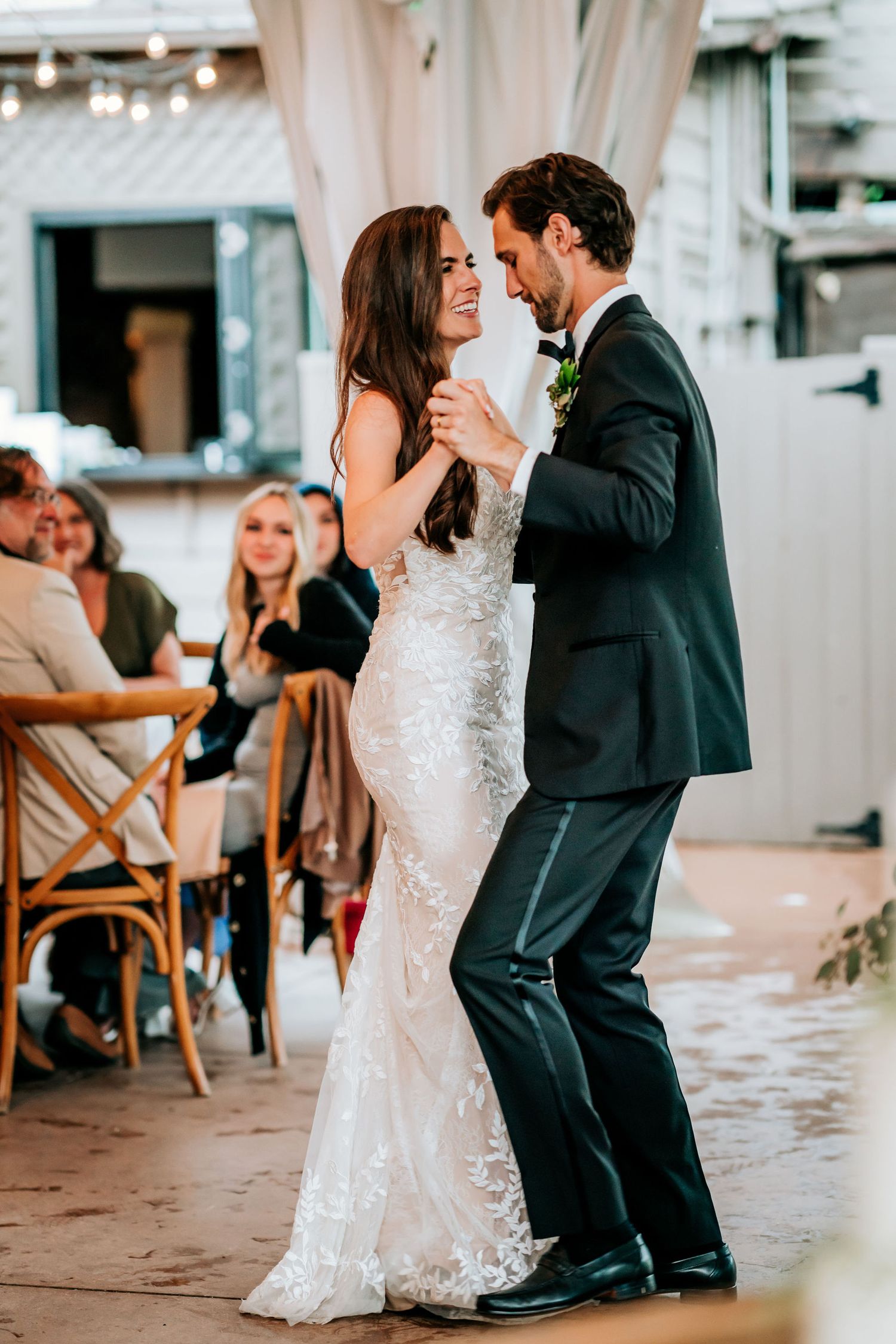 Couple sharing their first dance in elegant wedding attire on a covered patio.