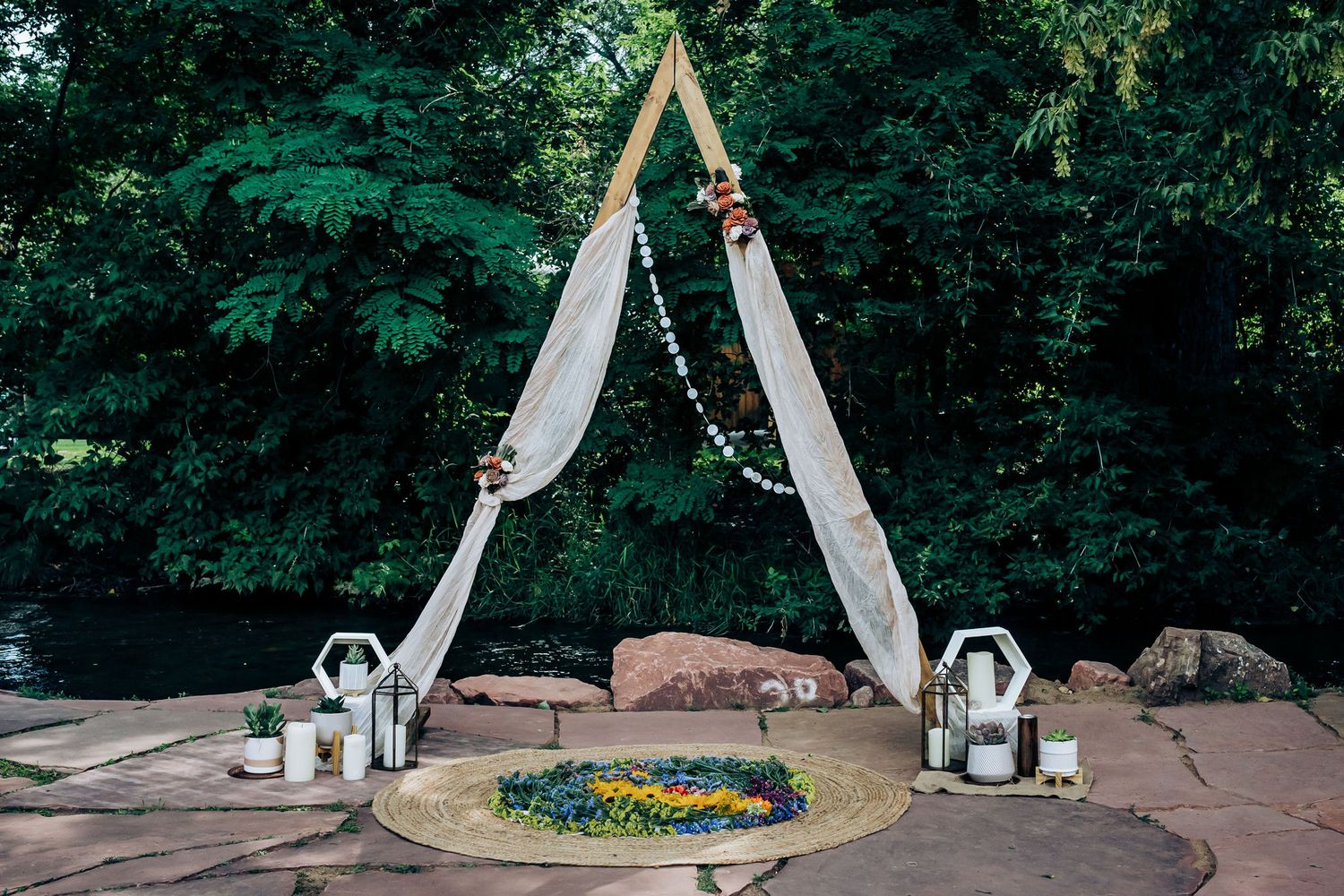 Elegant wedding arch with white draping and floral decorations set up on stone patio.