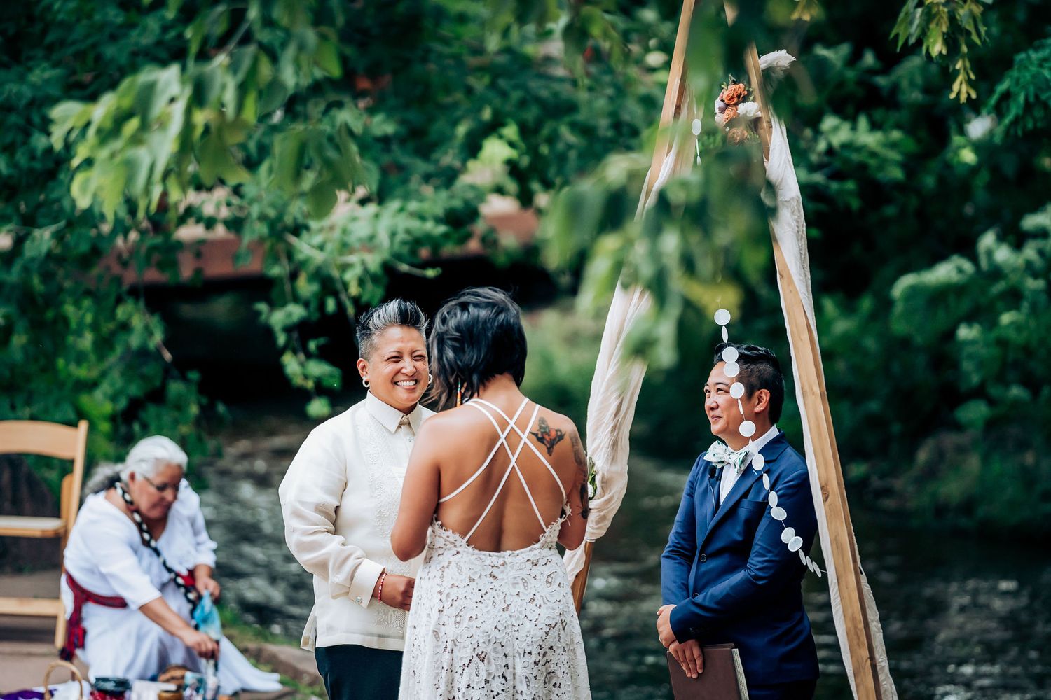 Wedding celebration under a wooden triangle arch with decorative white draping in nature.