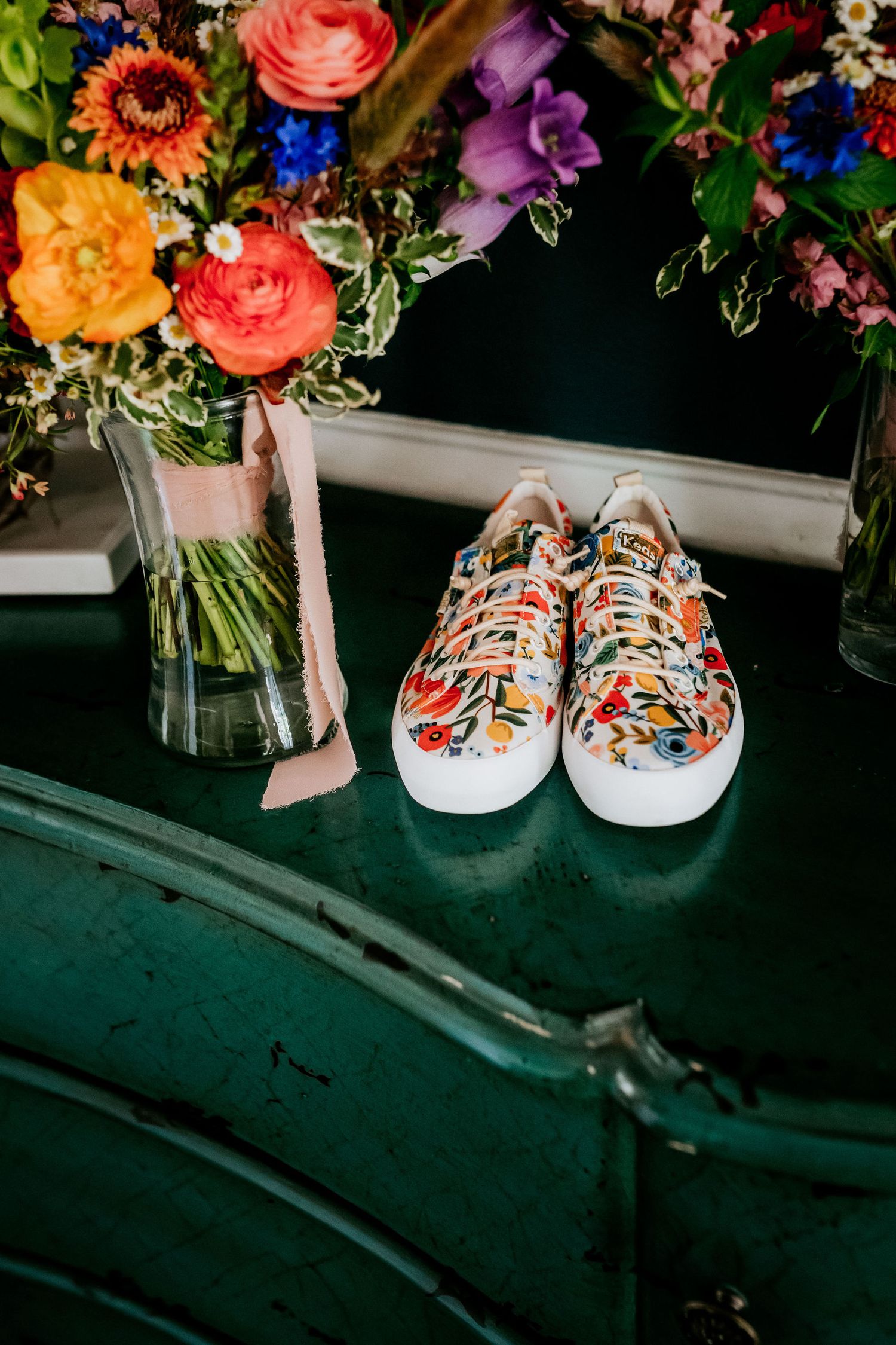 Floral-patterned sneakers displayed next to a vibrant bouquet of colorful flowers on a green surface.