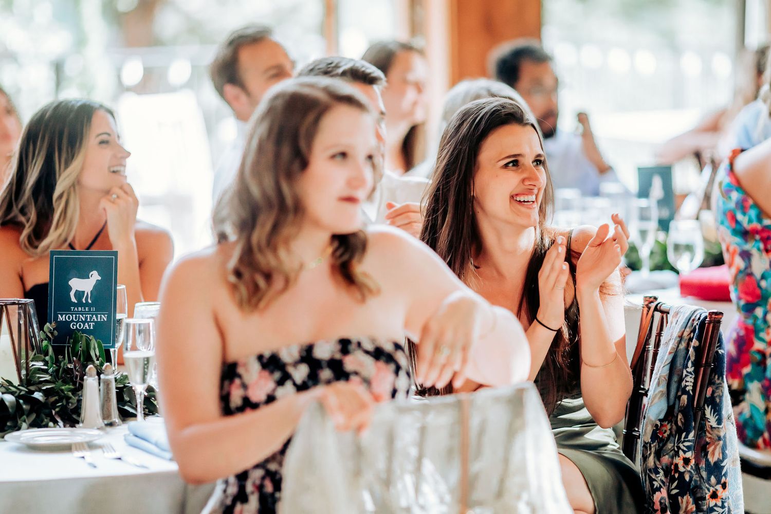 Wedding guests in formal attire react joyfully during a reception celebration at an indoor venue.