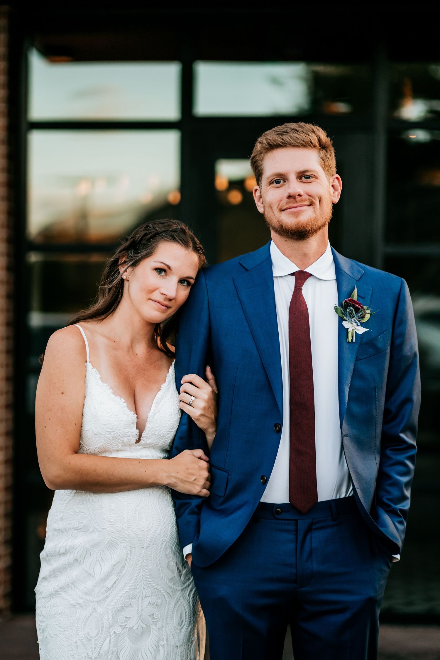 A couple poses against a brick wall backdrop at their wedding celebration.