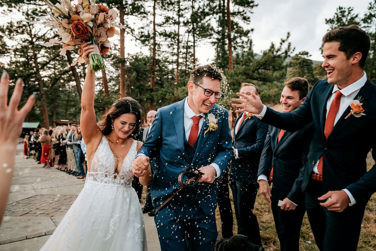 Joyful wedding celebration with confetti toss outside surrounded by wedding party members.