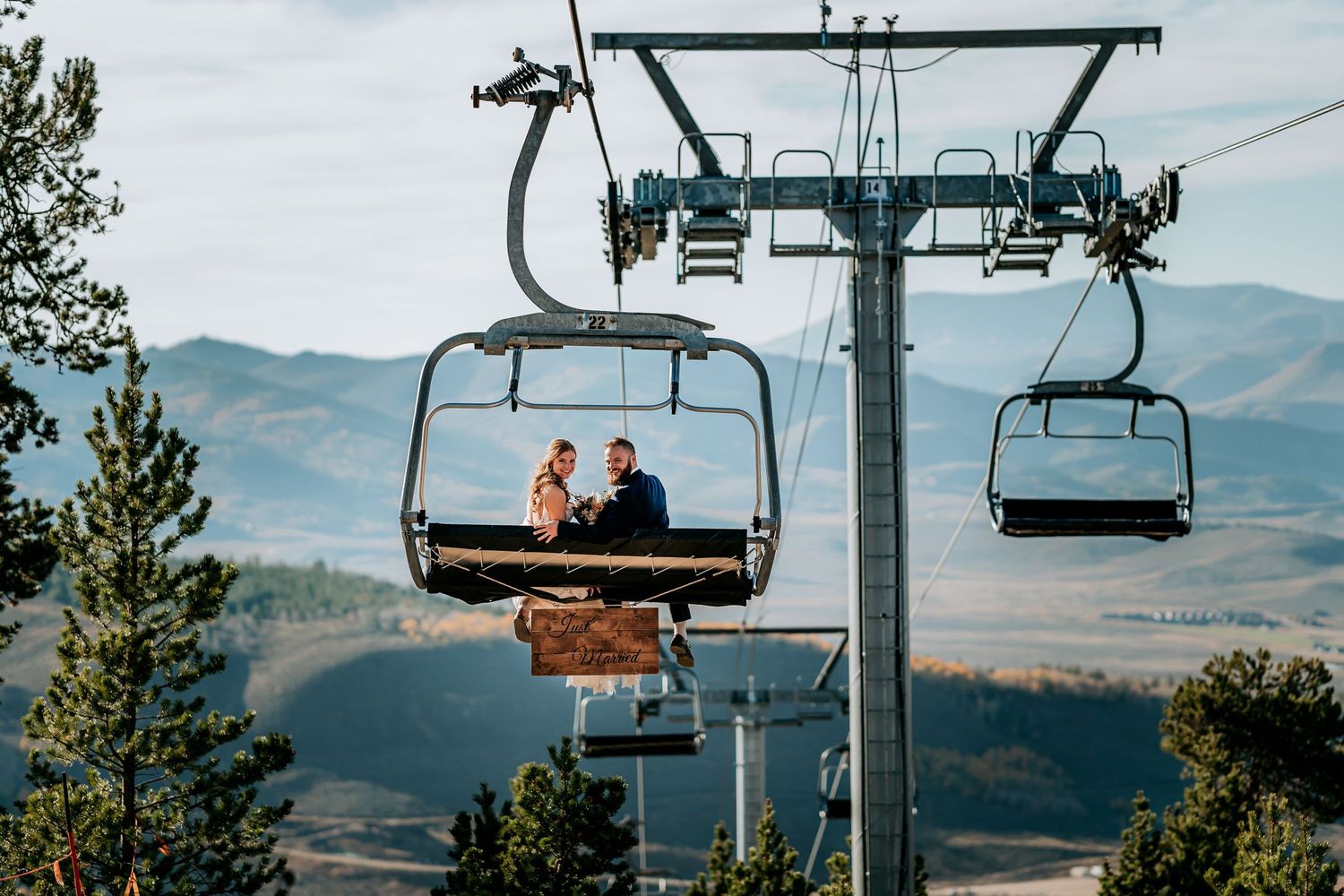 Scenic mountain landscape view from a chairlift showing multiple ski lift chairs against a backdrop of rolling hills.