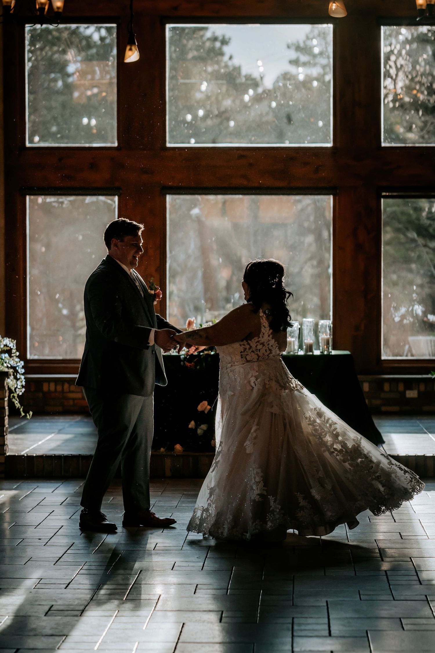 Romantic silhouette of a couple dancing in front of large windows during their wedding reception.
