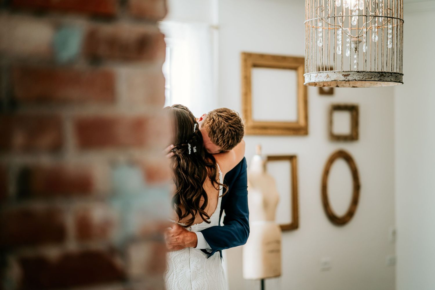 An intimate wedding moment captured in an indoor setting with chandelier lighting.