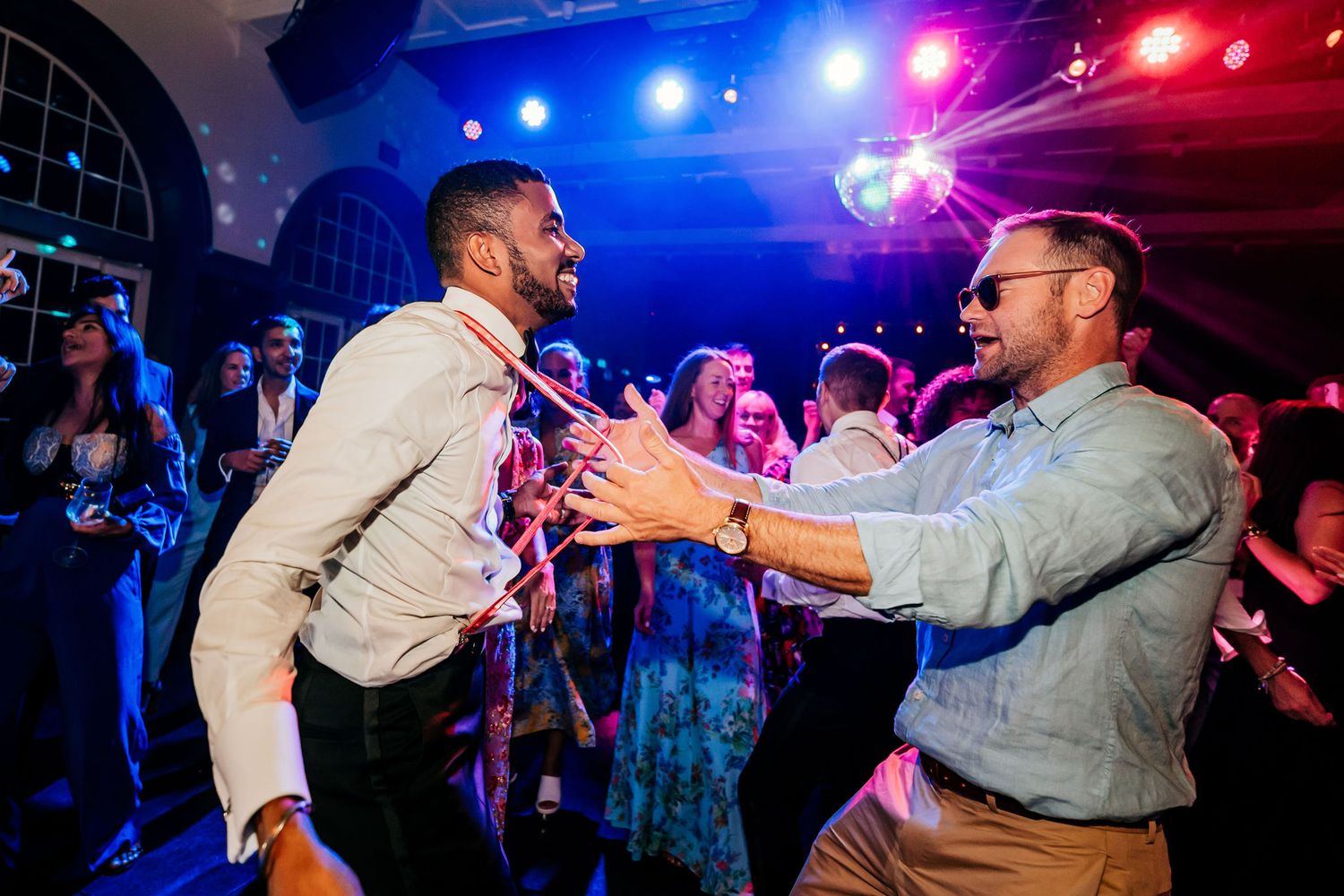 Two partygoers enthusiastically dancing together under vibrant blue and red spotlights.