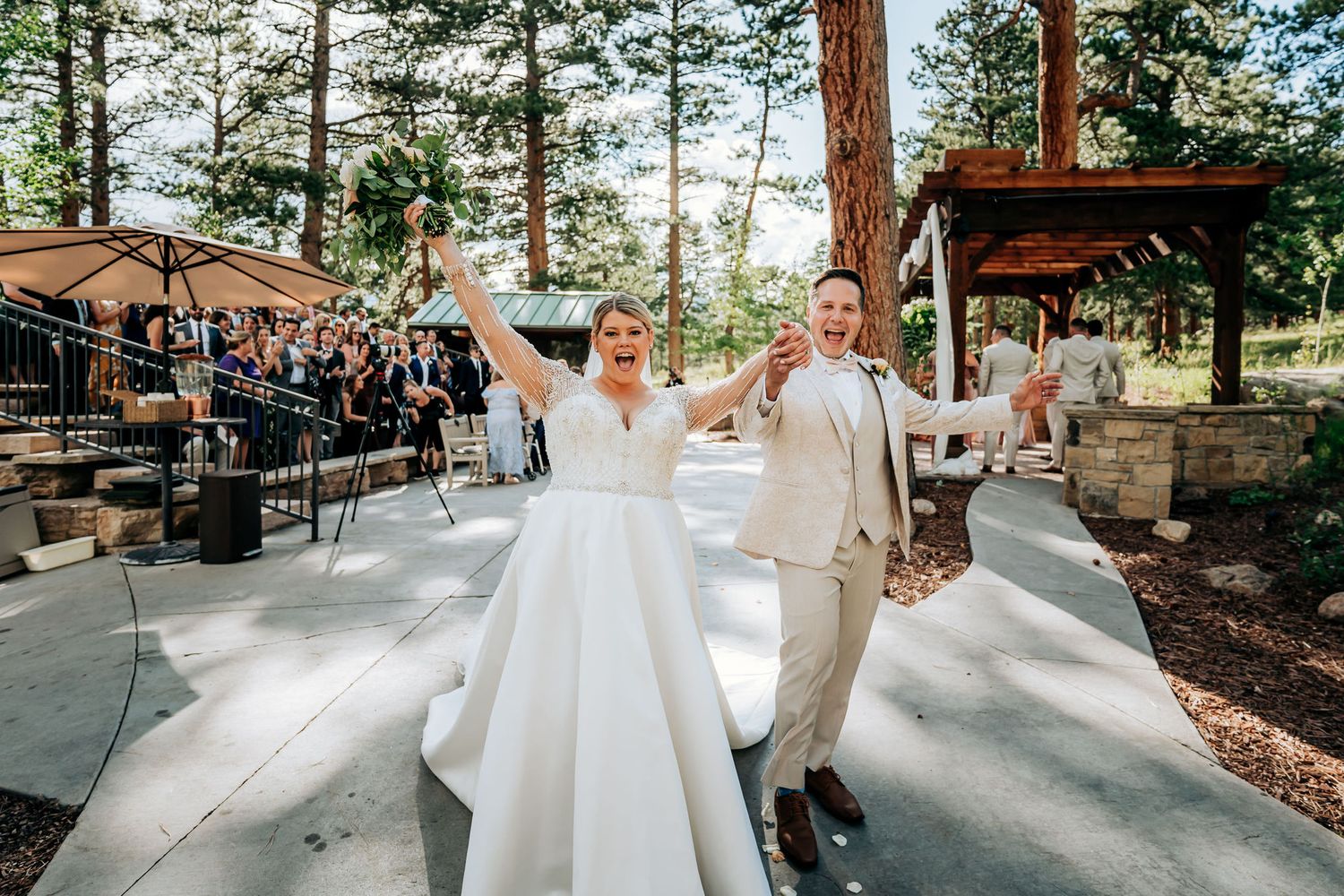 Wedding couple celebrating on an outdoor dance floor surrounded by pine trees.