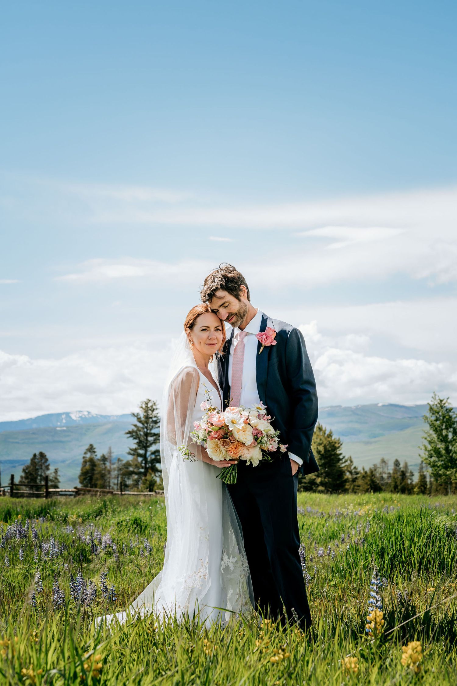 A romantic wedding couple embraces in a mountain meadow filled with wildflowers on a sunny day.