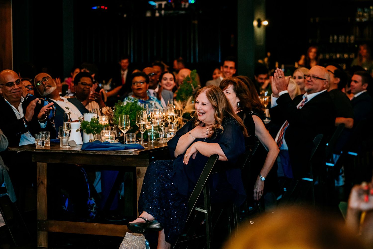 Candid reception scene with guests laughing at tables during evening celebration.