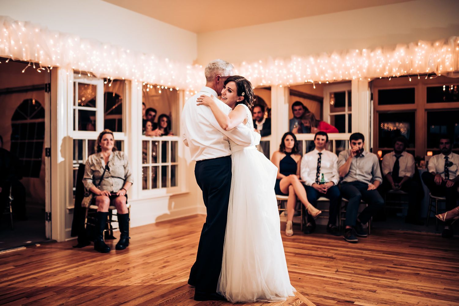 Newlyweds dance together on a hardwood floor while guests watch from the sidelines.