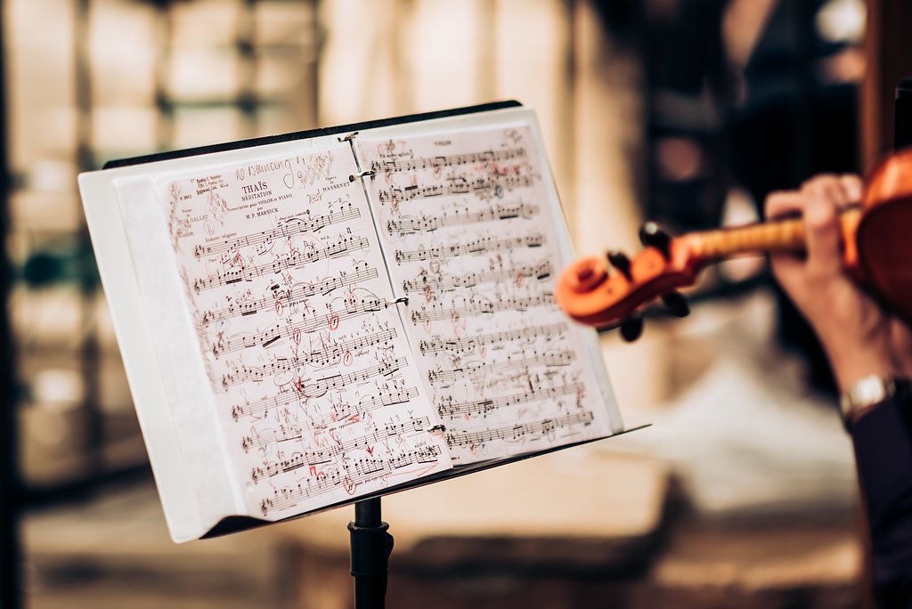 Sheet music on a music stand with a violinist playing in soft focus background.