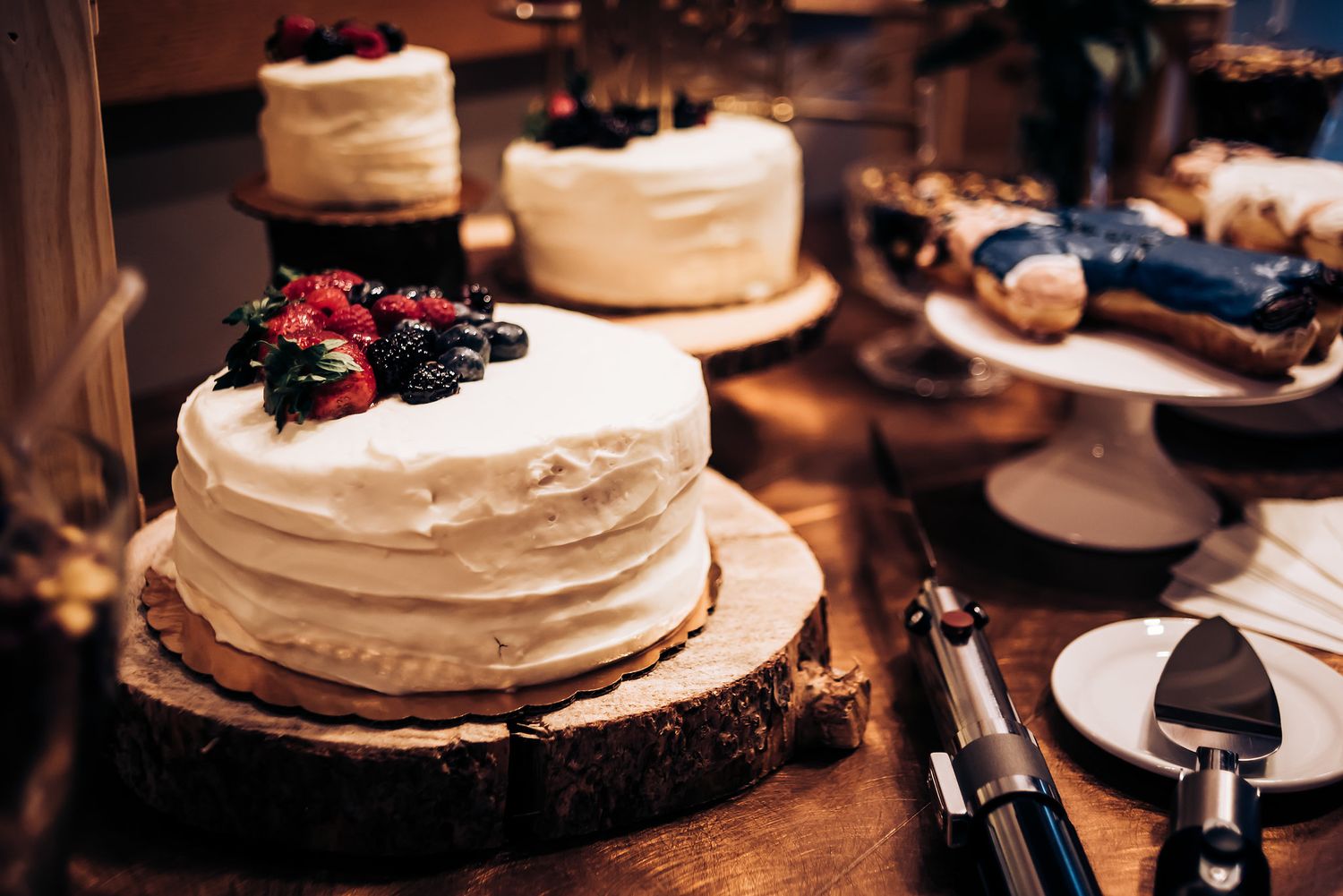 Elegant white wedding cakes topped with fresh berries displayed on wooden cake stands.