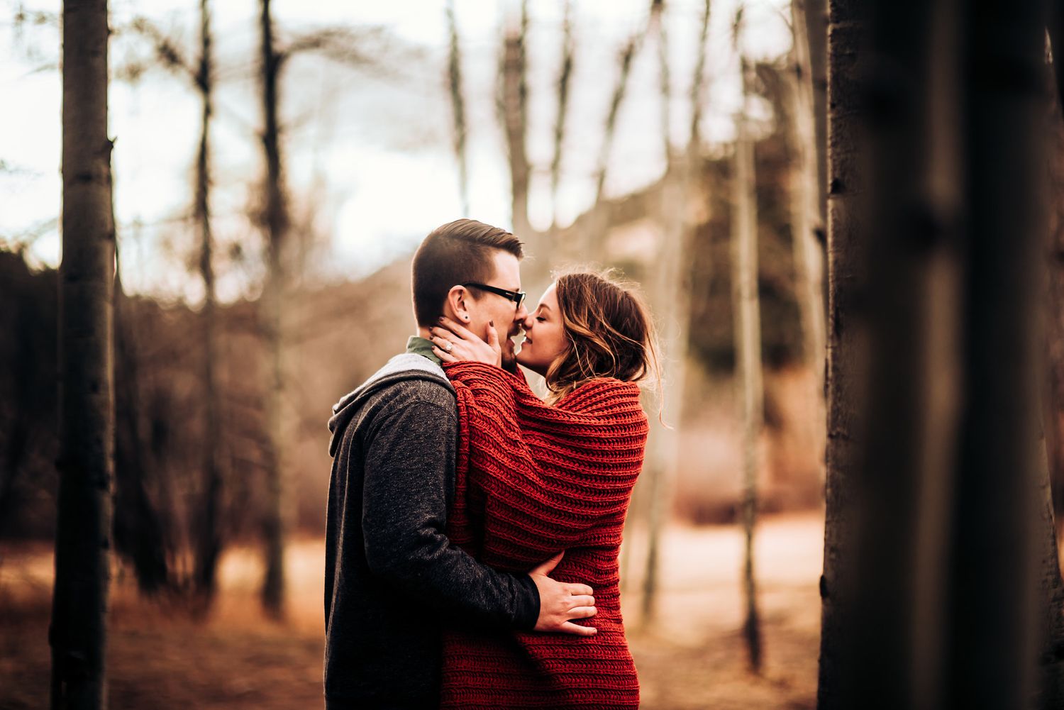 A couple embraces tenderly in an autumn forest setting.