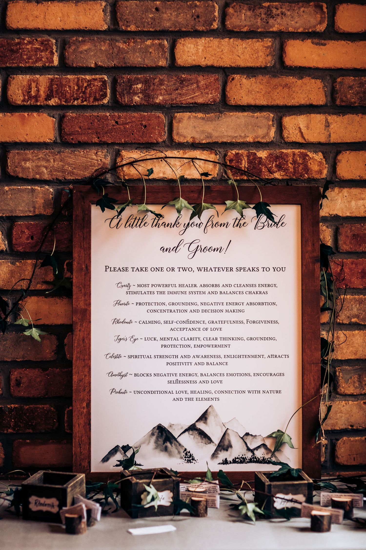 Wedding menu against rustic brick wall with mountain illustrations and greenery decor.