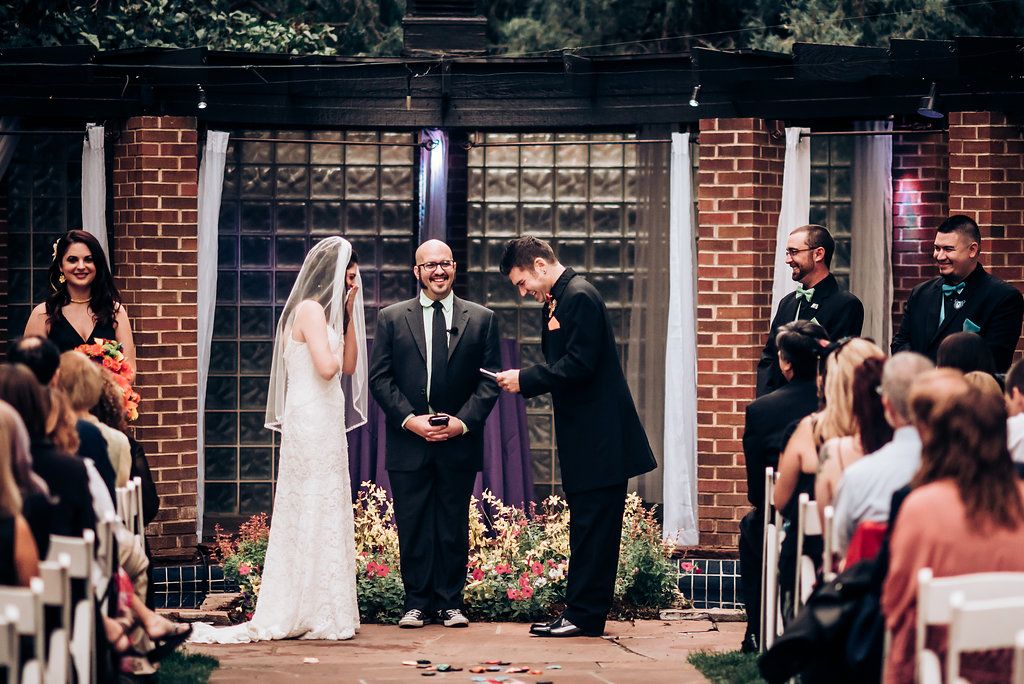 Wedding ceremony in progress at brick venue with decorative flowers and seated guests.