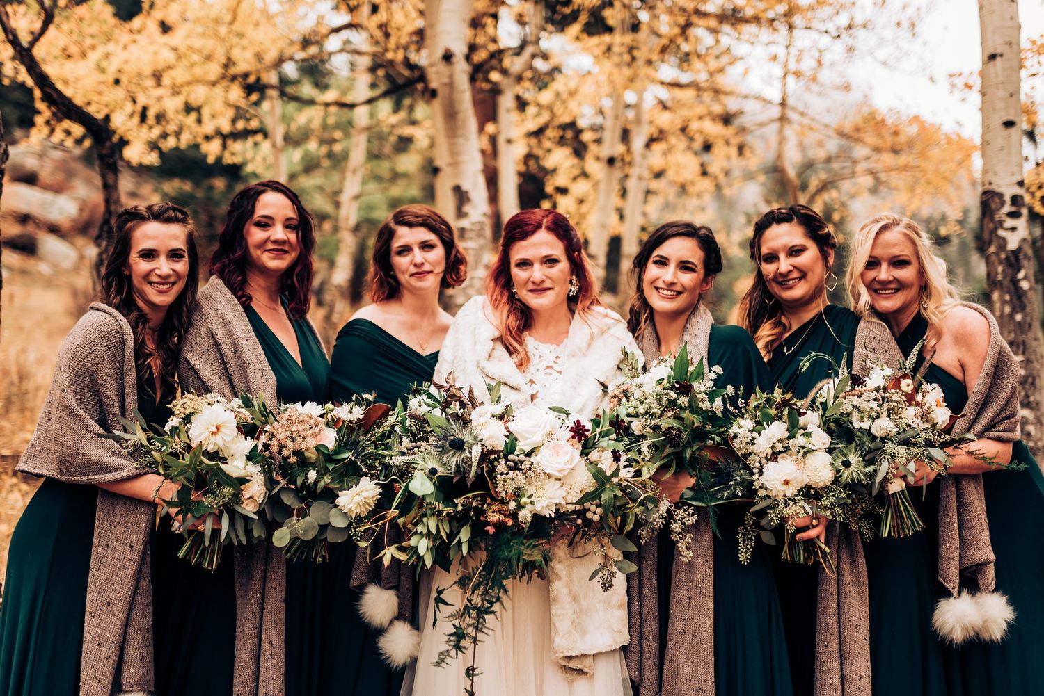 Bridal party holding lush white floral bouquets poses together in fall mountain setting.