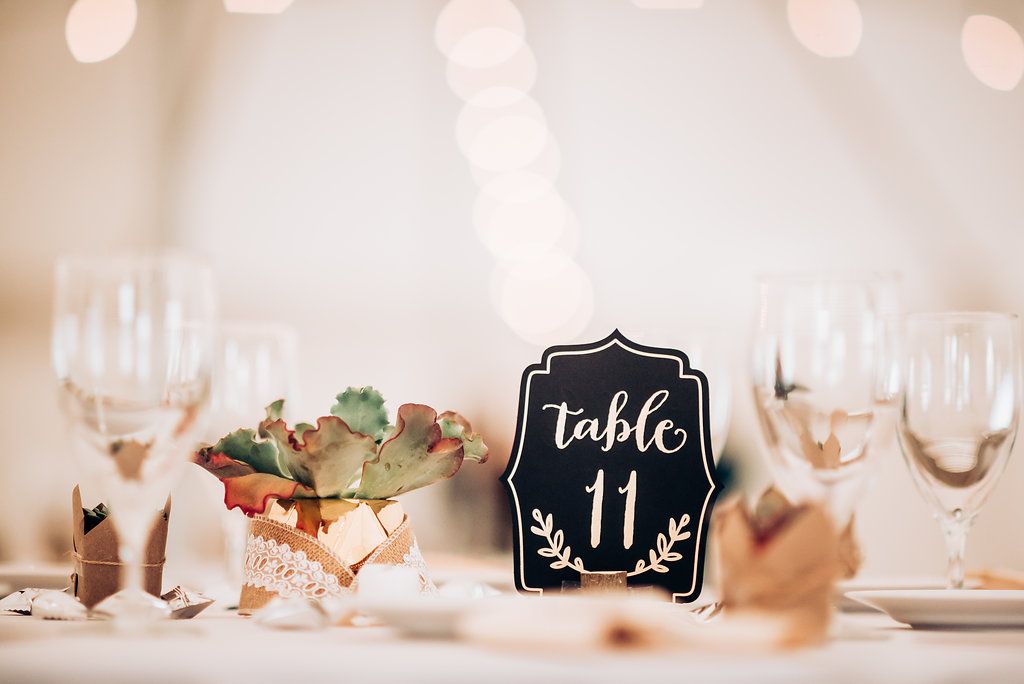 Elegant wedding table setting with a black table number sign, wine glasses and floral centerpiece.