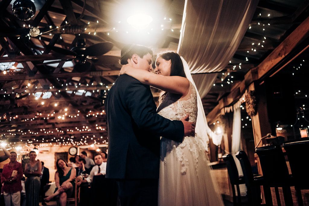 A romantic dance moment captured under warm string lights at an indoor wedding reception.