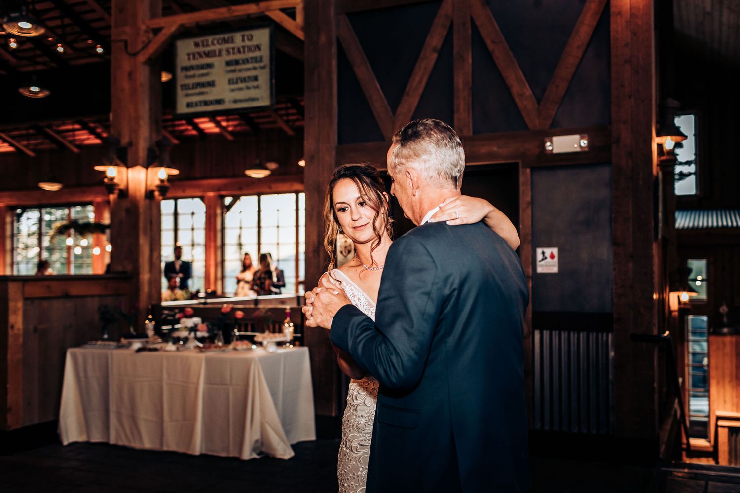 Couple dances intimately in rustic barn venue with string lights.