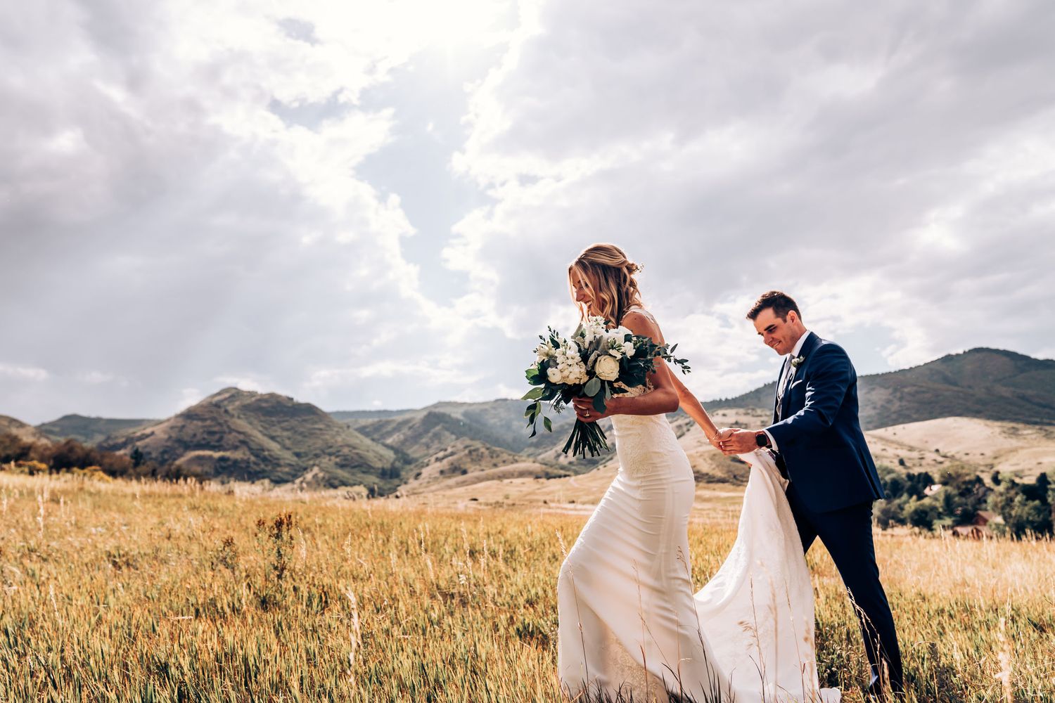 Couple dances in mountain meadow with dramatic cloudy sky and rolling hills.