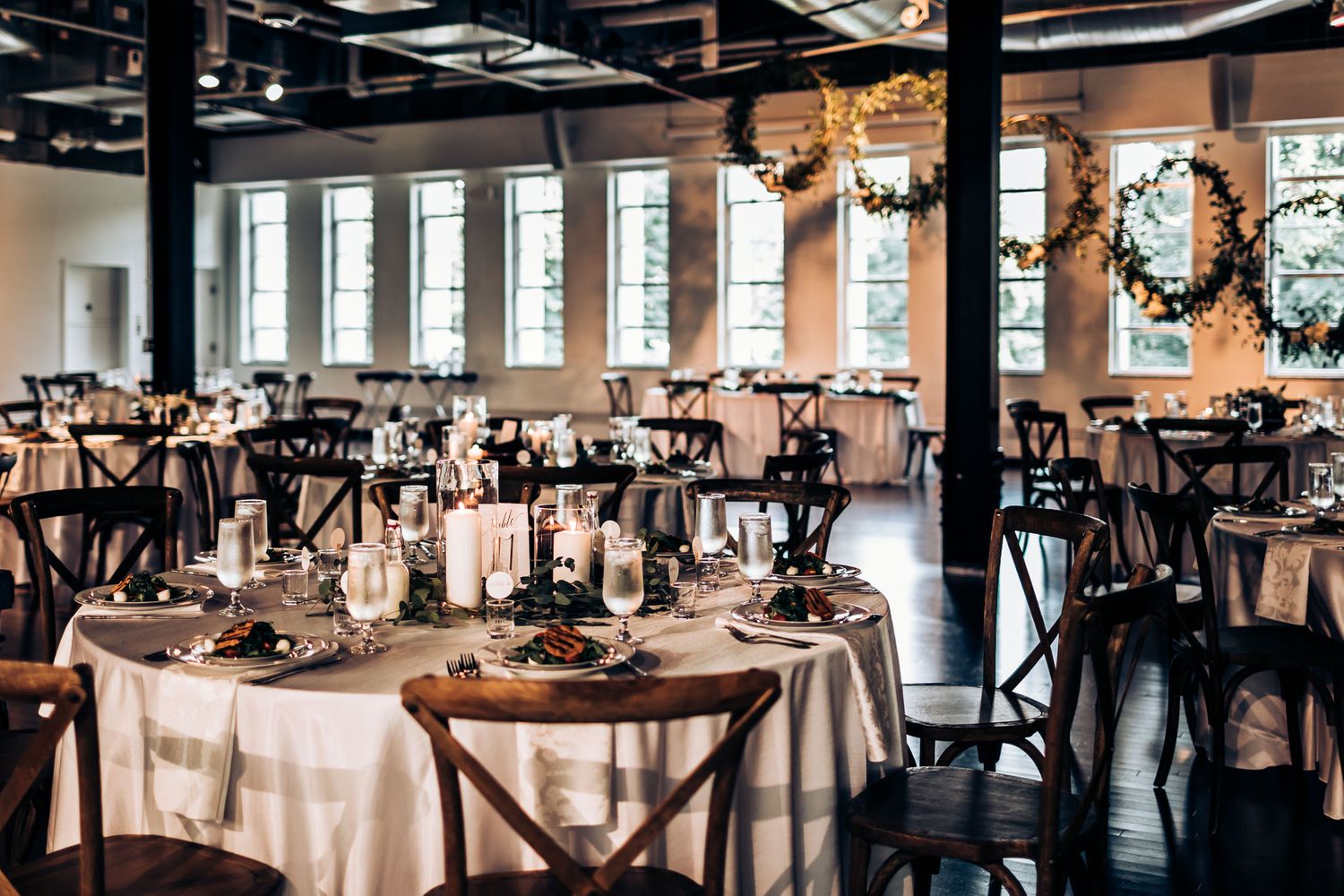 Modern industrial wedding reception venue with round tables and crossback chairs.