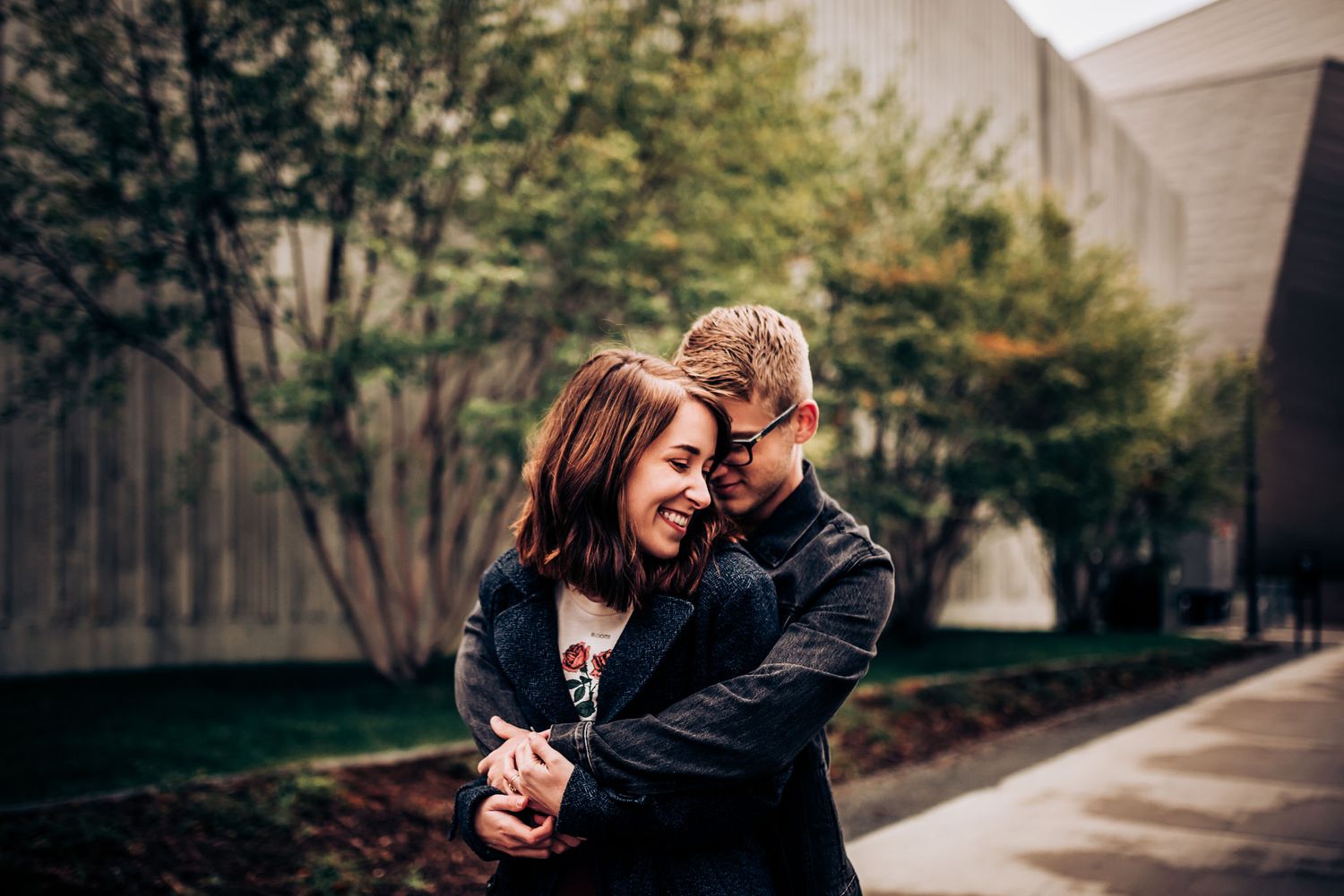 A couple shares a tender moment outdoors near modern architecture.