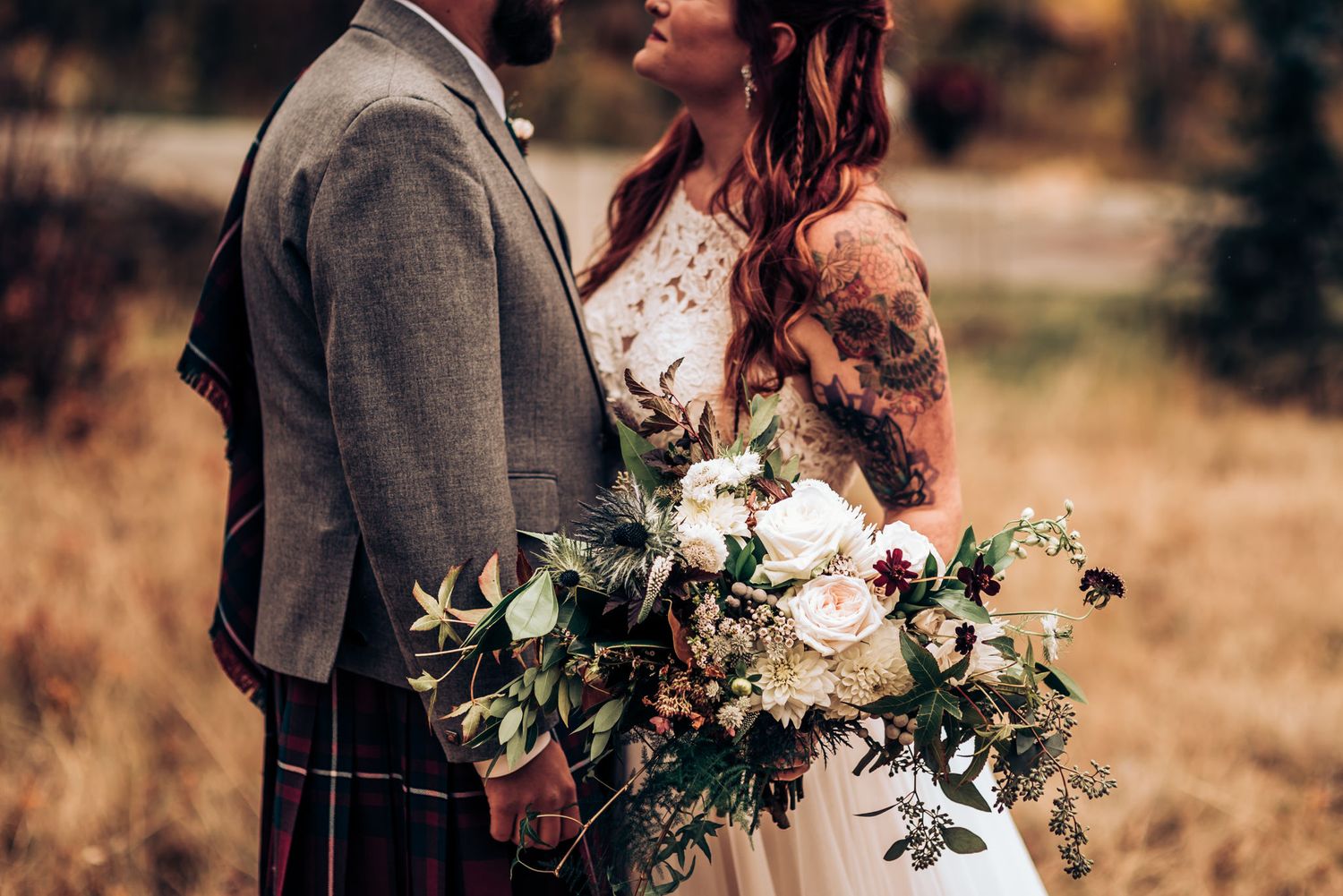 Close-up of wedding couple in Scottish attire with white floral bouquet.