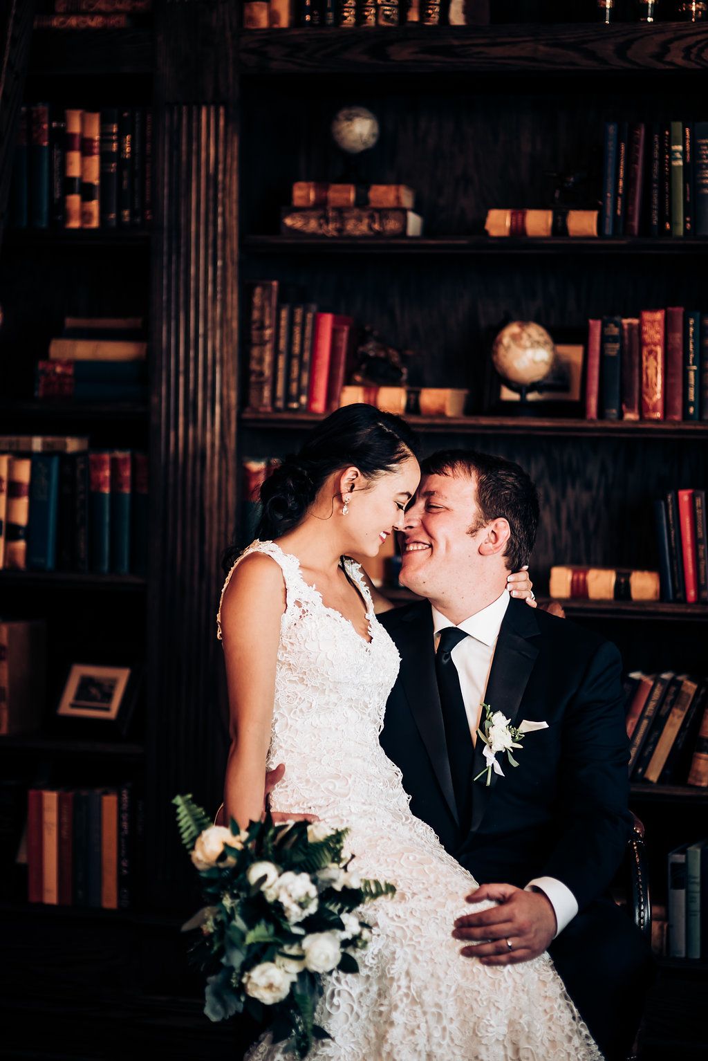 Intimate portrait of couple sharing tender moment in library setting with vintage bookshelves.