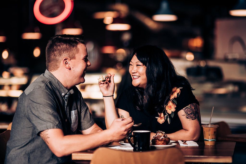 A couple sharing a laugh while enjoying dessert and drinks at a dimly lit restaurant.