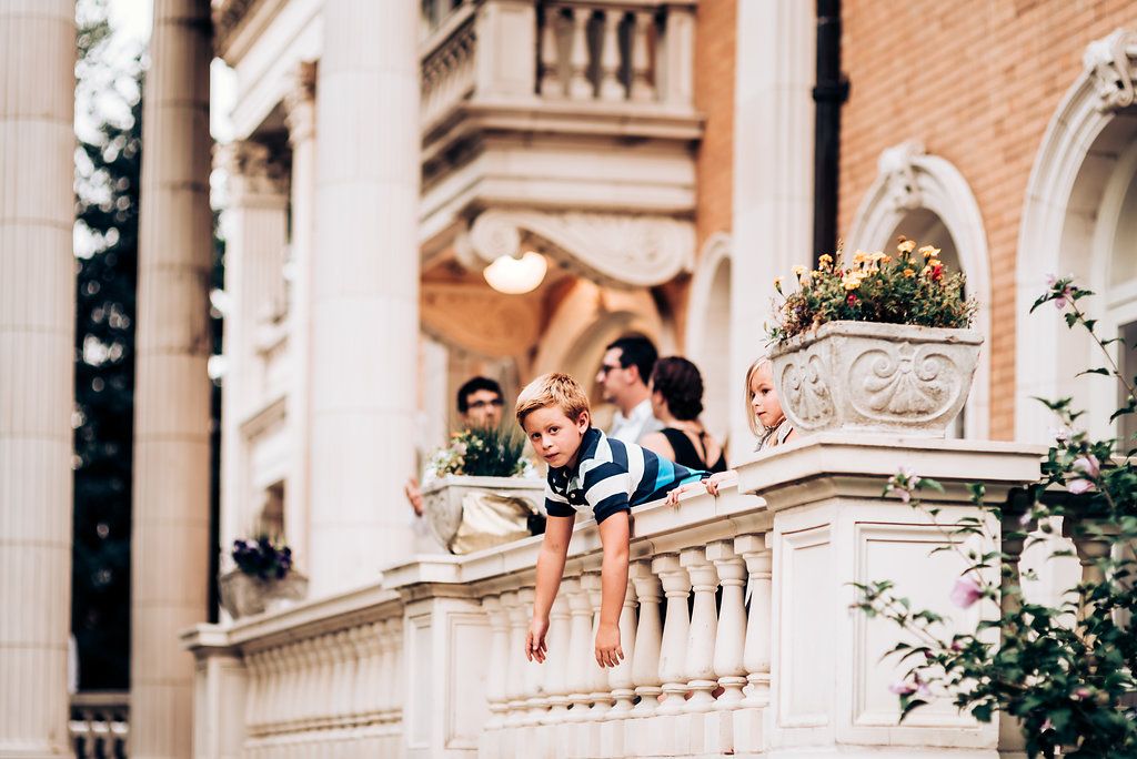 Guests lean over an ornate stone balcony at an elegant venue with classical architecture.
