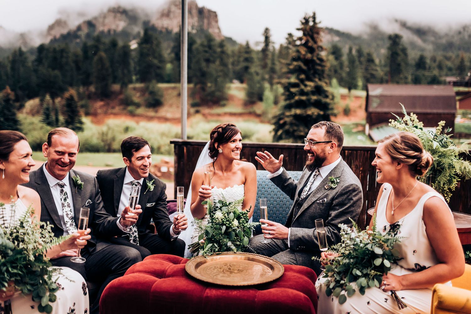 Wedding party enjoying drinks and conversation with mountain scenery in background.