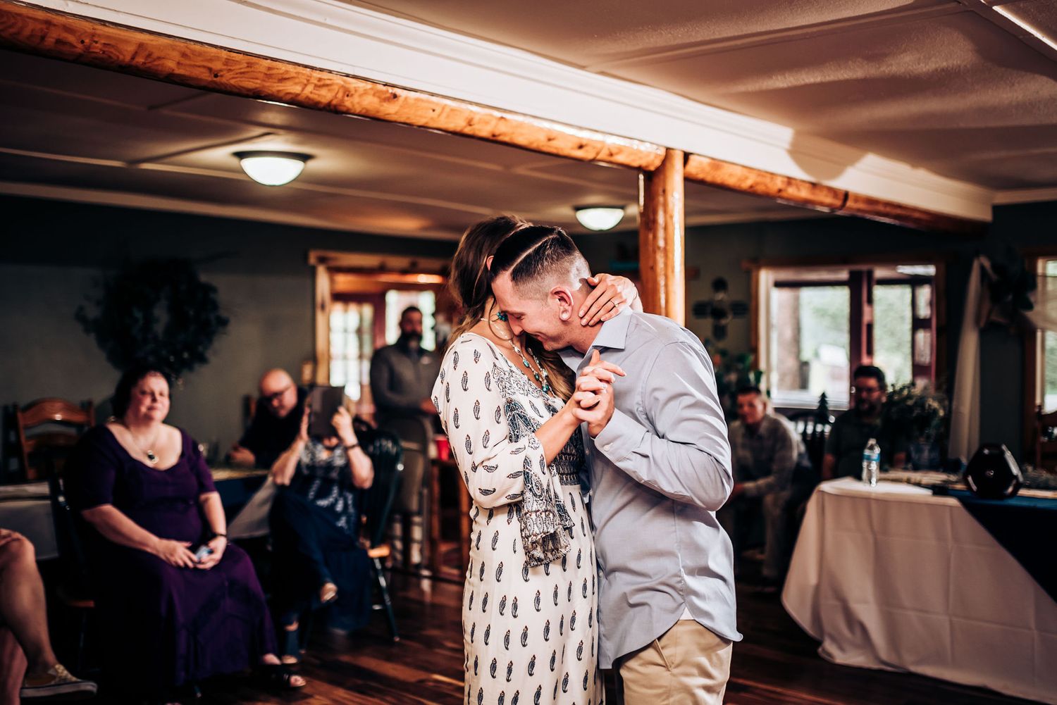 A couple shares an intimate slow dance in a reception hall decorated with string lights.