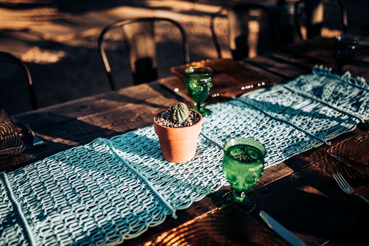 A rustic table setting with turquoise runner and green glassware alongside small potted cacti.