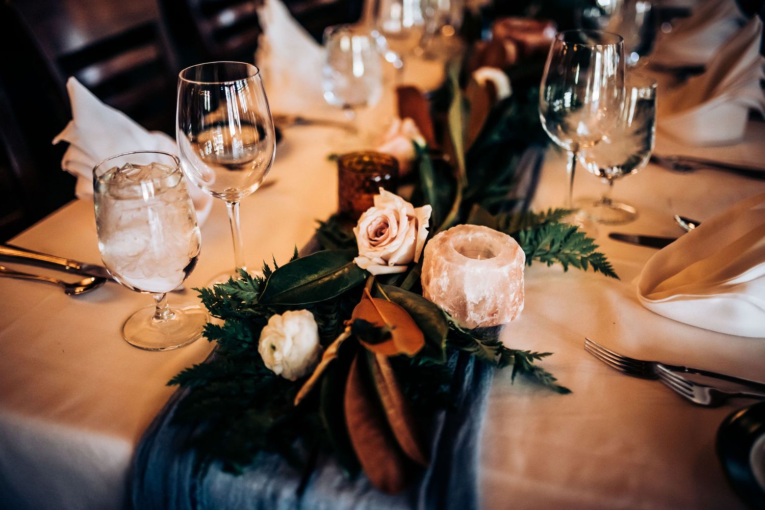 Elegant wedding table setting with wine glasses and pink rose centerpiece.