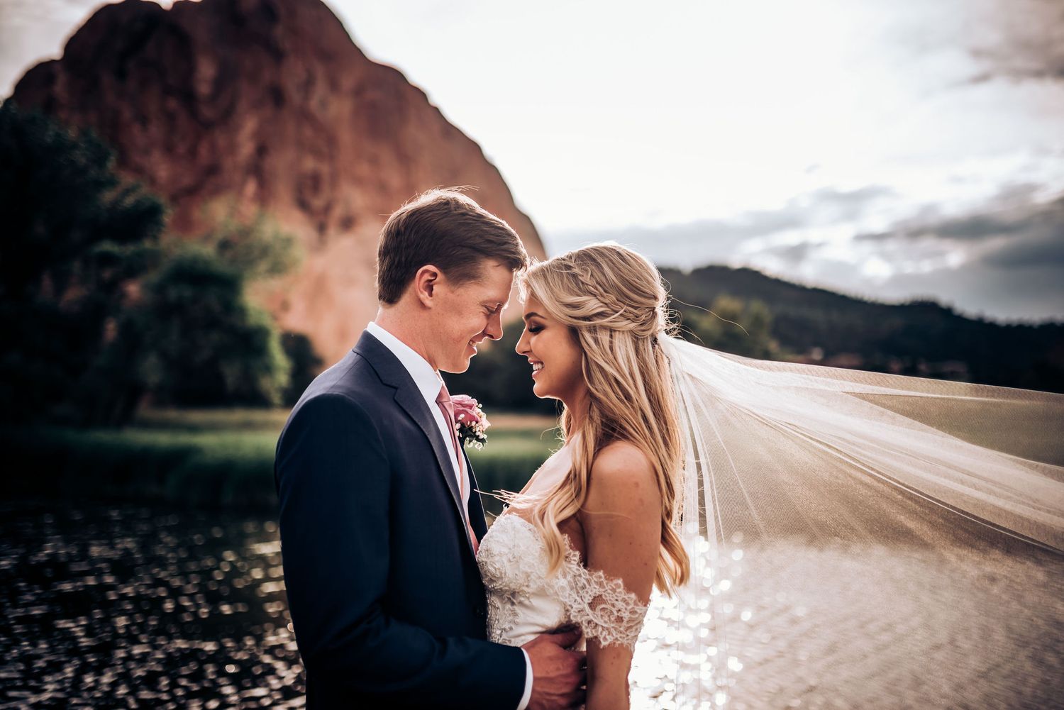 A romantic wedding photo capturing a couple in an intimate moment against dramatic red rock formations at sunset.
