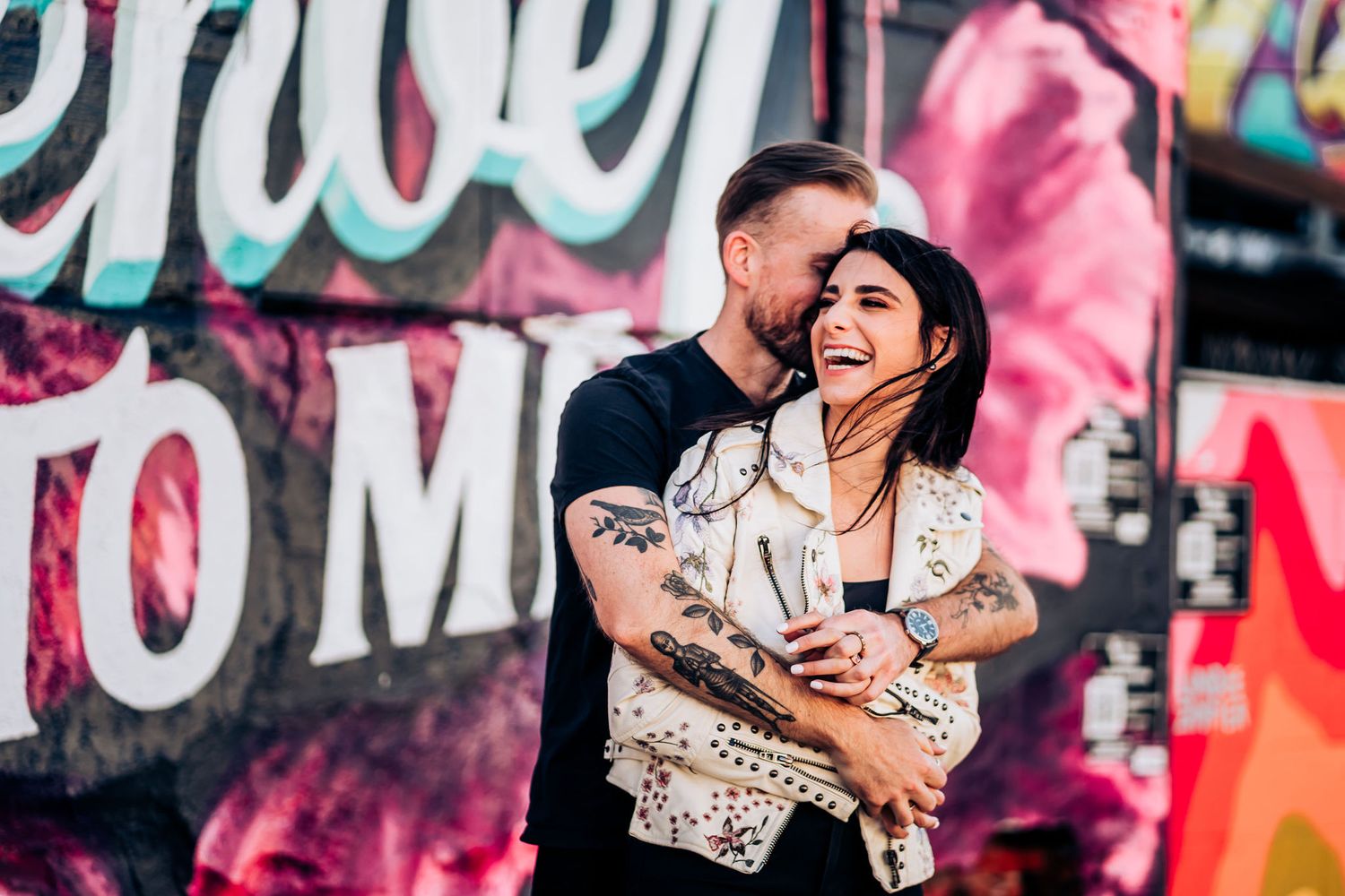 Couple shares intimate moment against vibrant street art mural background.